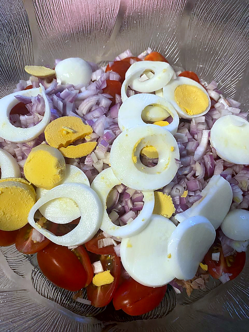 Boiled eggs, red onion and cherry tomatoes layered in a glass bowl for a tuna and potato salad