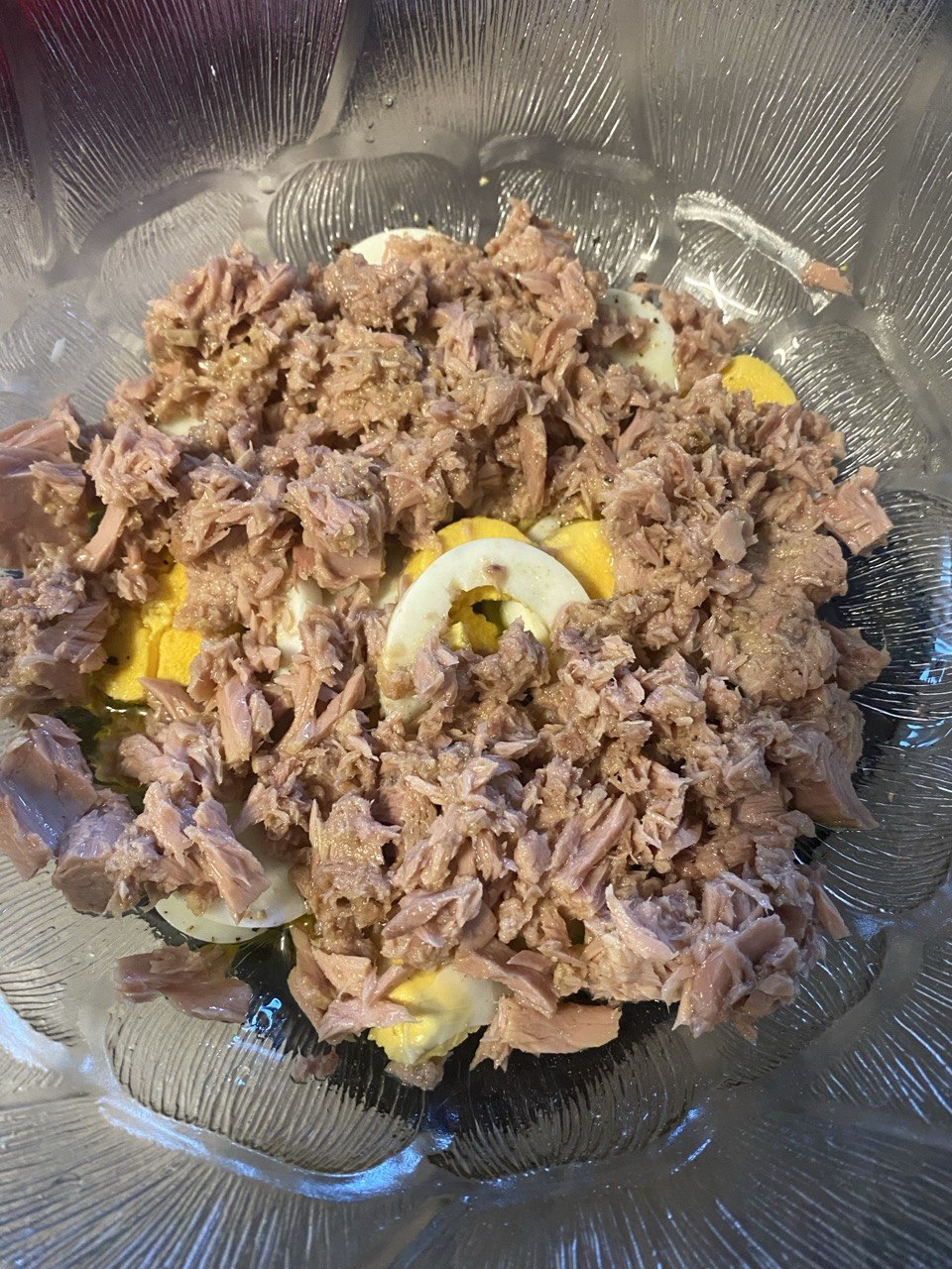 Flaked tuna added to boiled eggs, potatoes, red onion and cherry tomatoes in a glass bowl.