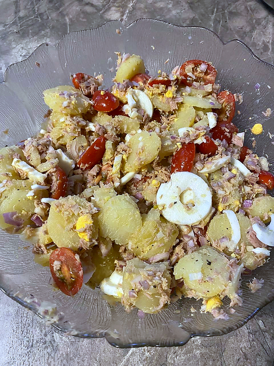 Finished tuna, egg and potato salad with cherry tomatoes, red onion and olive oil in a glass serving bowl.